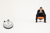 Photo : Anxious businessman sitting on chair with stopwatch showing time representing loss of time Anxious businessman sitting on chair with stopwatch showing time representing loss of time
