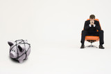 Photo: Worried businessman on chair and piggybank tied with rope representing financial difficulties Worried businessman on chair and piggybank tied with rope representing financial difficulties
