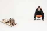 Photo: Model home on mouse trap with worried businessman sitting on chair representing increasing real estate rates Model home on mouse trap with worried businessman sitting on chair representing increasing real estate rates