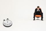 Photo : Worried businessman sitting on chair with stopwatch representing loss of time Worried businessman sitting on chair with stopwatch representing loss of time