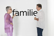 Photo: Couple discussing family issues against white wall with German text "Familie" Couple discussing family issues against white wall with German text "Familie"