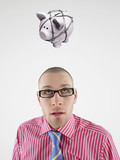 Photo: Young businessman looking up at piggy bank tied with rope representing trapped finances Young businessman looking up at piggy bank tied with rope representing trapped finances