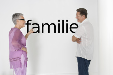 Photo: Couple discussing family issues against white wall with German text "Familie" Couple discussing family issues against white wall with German text "Familie"