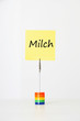 Photo: Sticky notepaper with German text "Milch" (milk) clipped to a multicolored card holder Sticky notepaper with German text "Milch" (milk) clipped to a multicolored card holder