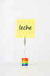 Photo: Sticky notepaper with Spanish text "leche" (Milk) clipped to a multicolored card holder Sticky notepaper with Spanish text "leche" (Milk) clipped to a multicolored card holder
