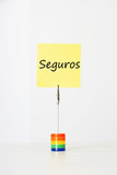 Photo: Sticky notepaper with Spanish text "seguros" (Insurance) clipped to a multicolored card holder Sticky notepaper with Spanish text "seguros" (Insurance) clipped to a multicolored card holder