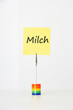 Photo: Sticky notepaper with German text "Milch" (milk) clipped to a multicolored card holder Sticky notepaper with German text "Milch" (milk) clipped to a multicolored card holder