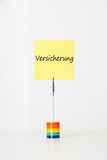 Photo: Sticky notepaper with German text "Versicherung" (Insurance) clipped to a multicolored card holder Sticky notepaper with German text "Versicherung" (Insurance) clipped to a multicolored card holder