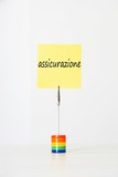 Photo: Sticky notepaper with Italian text "assicurazione" (Insurance) clipped to a multicolored card holder Sticky notepaper with Italian text "assicurazione" (Insurance) clipped to a multicolored card holder