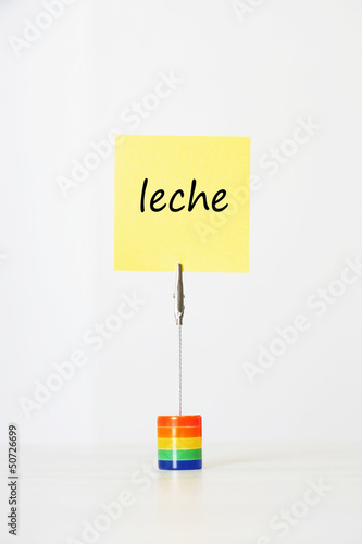 Photo: Sticky notepaper with Spanish text "leche" (Milk) clipped to a multicolored card holder Sticky notepaper with Spanish text "leche" (Milk) clipped to a multicolored card holder