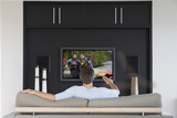 Photo: Back view of mid-adult man changing channels with television remote control in living room Back view of mid-adult man changing channels with television remote control in living room