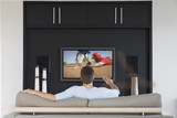 Photo: Back view of mid-adult man changing channels with television remote control in living room Back view of mid-adult man changing channels with television remote control in living room