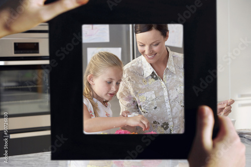Photo: Female hand framing mother and daughter baking together in kitchen Female hand framing mother and daughter baking together in kitchen