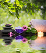 two candles and towels black stones and purple flower on water