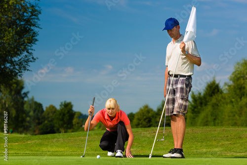 Photo: Young sportive couple playing golf on a course Young sportive couple playing golf on a course