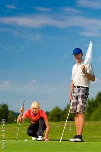 Photo: Young sportive couple playing golf on a course Young sportive couple playing golf on a course