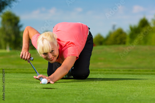 Photo: Young female golf player on course aiming for put Young female golf player on course aiming for put