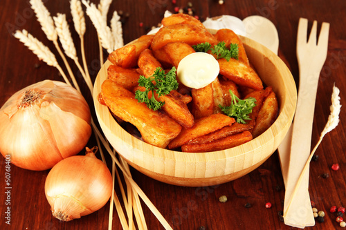 Photo: Appetizing village potatoes in bowl on wooden table close-up Appetizing village potatoes in bowl on wooden table close-up