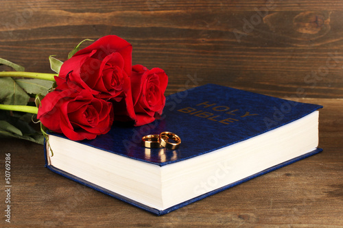 Photo: Wedding rings on bible with roses on wooden background Wedding rings on bible with roses on wooden background