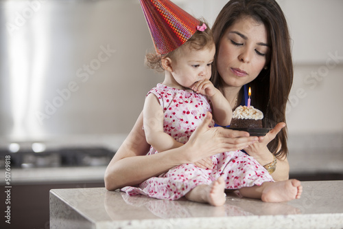 Photo: Cute baby girl and her mom blowing the candle of a birthday cake Cute baby girl and her mom blowing the candle of a birthday cake