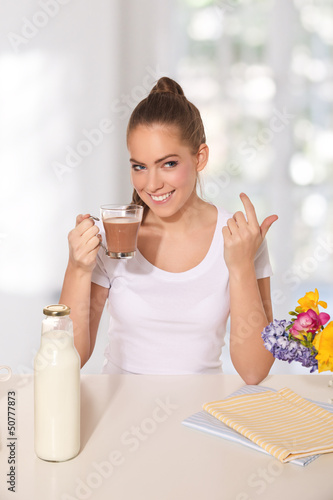 Photo: Young beautiful woman drinking a glass of hot drink while making Young beautiful woman drinking a glass of hot drink while making