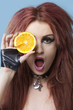 Photo: Portrait of funky young woman covering eye with sliced orange over blue background Portrait of funky young woman covering eye with sliced orange over blue background
