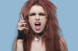Photo: Portrait of funky young woman screaming while using cell phone over blue background Portrait of funky young woman screaming while using cell phone over blue background