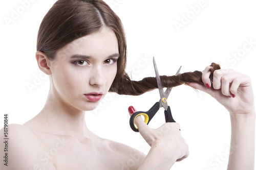 Photo: Portrait of beautiful young woman with scissors cutting her hair over white background Portrait of beautiful young woman with scissors cutting her hair over white background