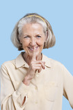 Photo: Portrait of smiling senior woman in casuals with finger on lips against blue background Portrait of smiling senior woman in casuals with finger on lips against blue background