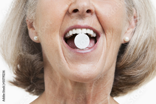 Photo: Senior woman with a pill between her teeth against white background Senior woman with a pill between her teeth against white background