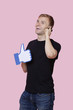 Foto: Cheerful young man using cell phone while holding fake like button over pink background Cheerful young man using cell phone while holding fake like button over pink background
