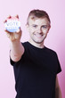 Photo: Portrait of a young man holding a VOTE badge up to the camera against pink background Portrait of a young man holding a VOTE badge up to the camera against pink background