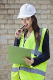 Photo: Portrait of a happy female supervisor with clipboard standing at construction site Portrait of a happy female supervisor with clipboard standing at construction site