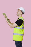 Photo: Side view of a male construction worker with clipboard looking away over pink background Side view of a male construction worker with clipboard looking away over pink background