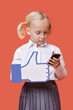 Photo: Young schoolgirl with cell phone holding fake like button against orange background Young schoolgirl with cell phone holding fake like button against orange background