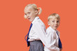 Photo: Happy young boy and girl in school uniform standing back to back over orange background Happy young boy and girl in school uniform standing back to back over orange background