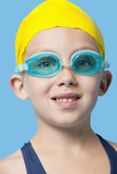 Photo: Close-up portrait of a happy young girl wearing swim cap and goggles over blue background Close-up portrait of a happy young girl wearing swim cap and goggles over blue background
