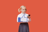 Foto: Portrait of a young schoolgirl with cell phone holding fake like button over orange background Portrait of a young schoolgirl with cell phone holding fake like button over orange background