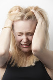 Photo: Frustrated young Caucasian woman with hands in hair against white background Frustrated young Caucasian woman with hands in hair against white background