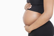 Photo: Mid section of young pregnant woman with hands on stomach over white background Mid section of young pregnant woman with hands on stomach over white background