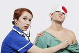 Photo : Portrait of female nurse treating an injured male patient against gray background Portrait of female nurse treating an injured male patient against gray background