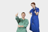 Photo : Portrait of young male patient with female nurse gesturing thumbs up against gray background Portrait of young male patient with female nurse gesturing thumbs up against gray background