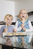 Photo: Portrait of happy boy with sister tasting spatula mix with cookie batter in kitchen Portrait of happy boy with sister tasting spatula mix with cookie batter in kitchen