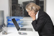 Photo: Side view of tired senior businesswoman in front of laptop at desk in office Side view of tired senior businesswoman in front of laptop at desk in office