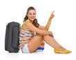Happy young tourist woman sitting near wheel bag