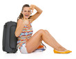 Smiling young tourist woman sitting near wheel bag