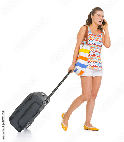 Photo: Happy tourist woman with wheel bag walking and talking mobile Happy tourist woman with wheel bag walking and talking mobile