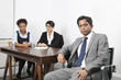 Photo: Portrait of Asian male with female colleagues in background at desk in office Portrait of Asian male with female colleagues in background at desk in office