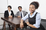 Photo: Portrait of African American female with colleagues in background at desk in office Portrait of African American female with colleagues in background at desk in office