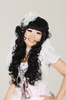 Photo: Portrait of cute happy young woman in doll costume posing over gray background Portrait of cute happy young woman in doll costume posing over gray background